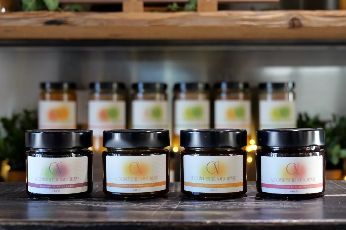 Quatre pots de confiture de la Conserverie Naborienne alignés devant des bocaux de compote